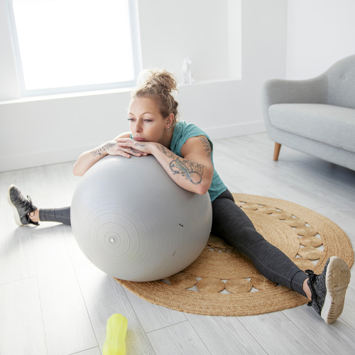 a woman stretching with an exercise ball in her living room, exercising to help improve her mental health